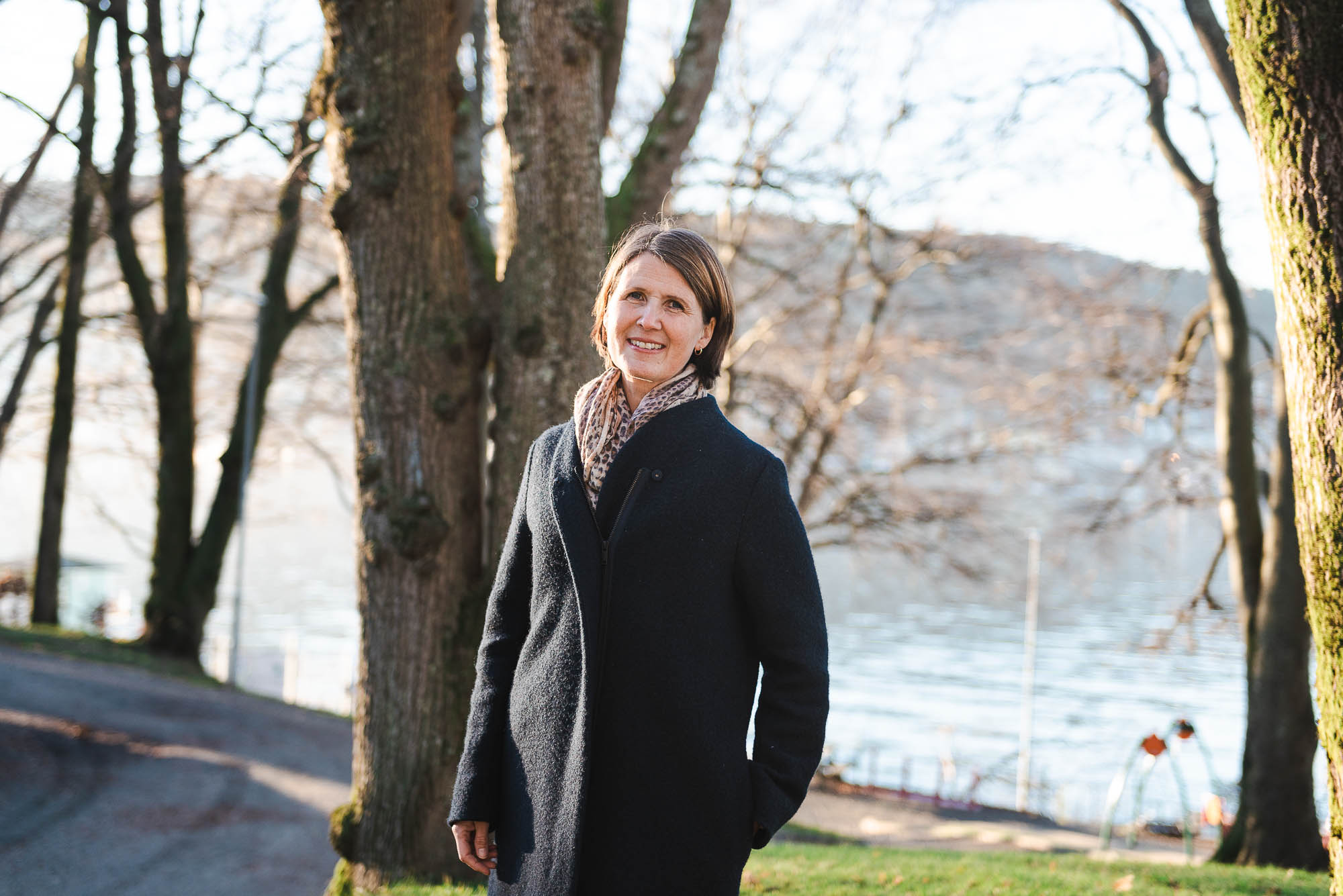 kvinne i kåpe ser mot kamera, ute i høstsol