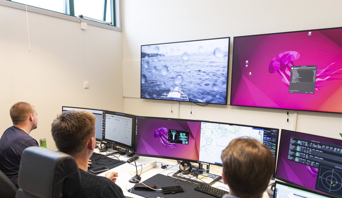 
Tre mennesker sitter inne i et rom og ser på åtte forskjellige skjermer.