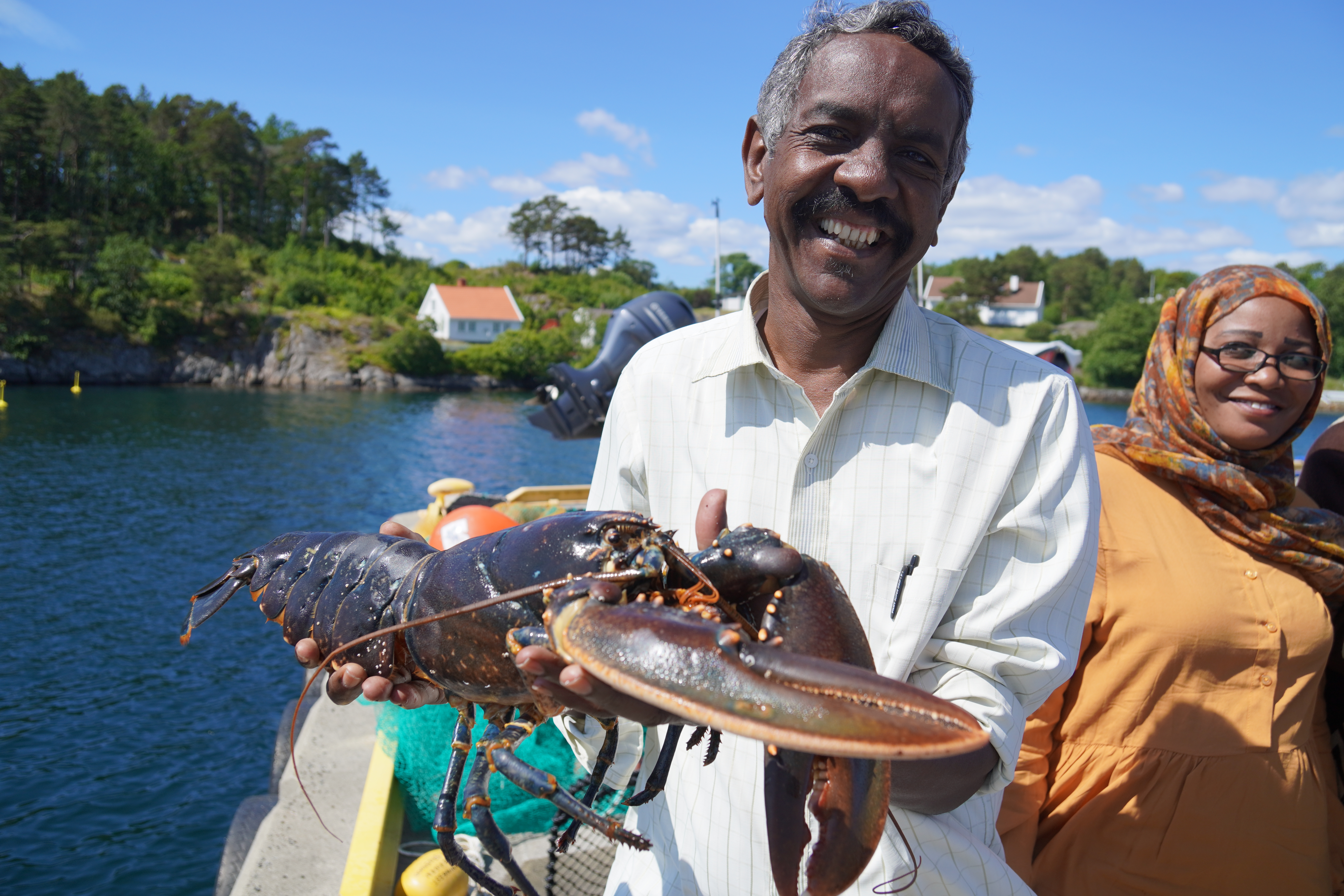 En av prosjektdeltagerne fra Sudan løfter opp hummer mot kamera og smiler bredt, mens meddeltager smiler lurt bak ryggen hans.