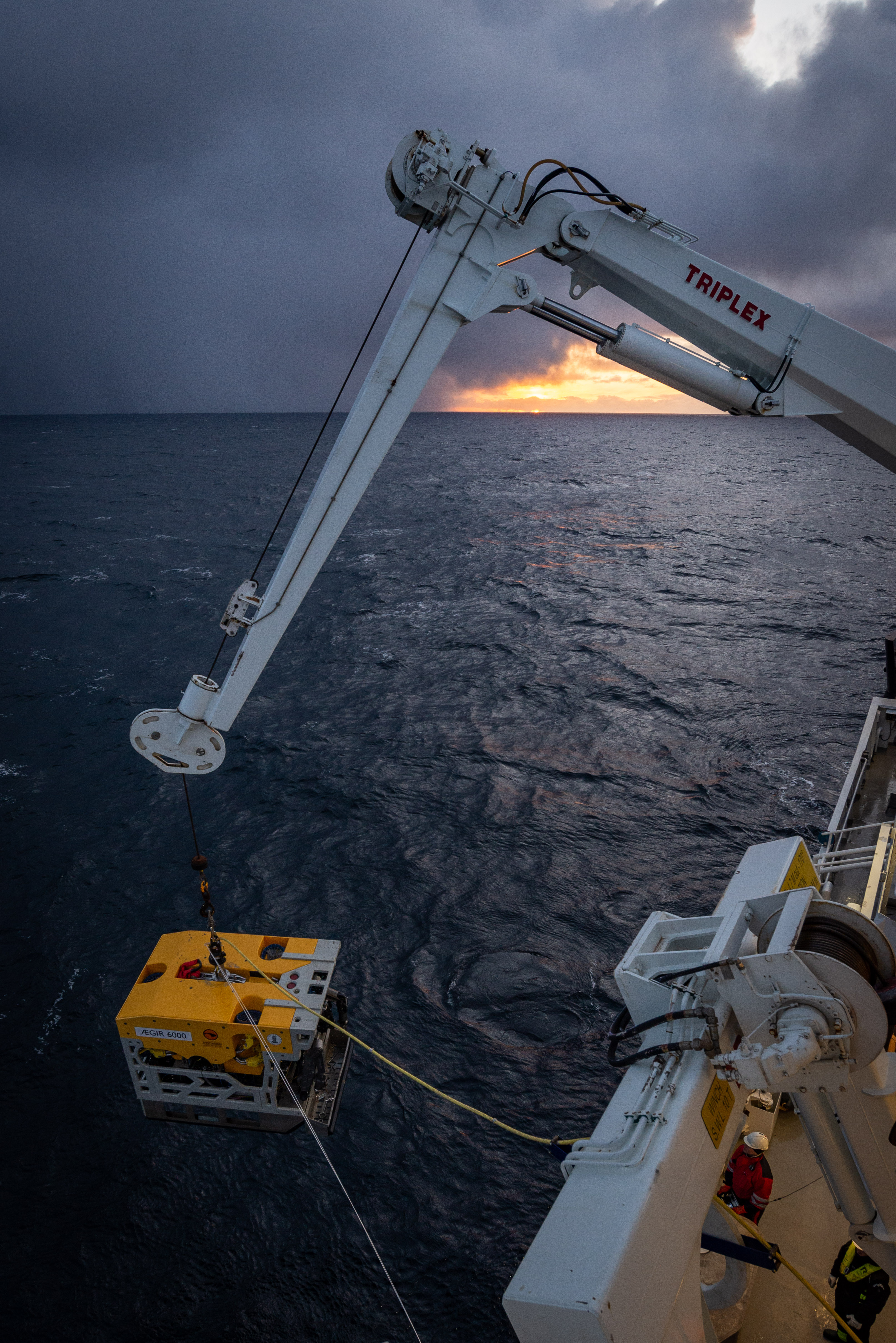 Undervannsroboten Ægir 6000, i form av en firkantet gul boks, senkes i sjøen fra skipet.