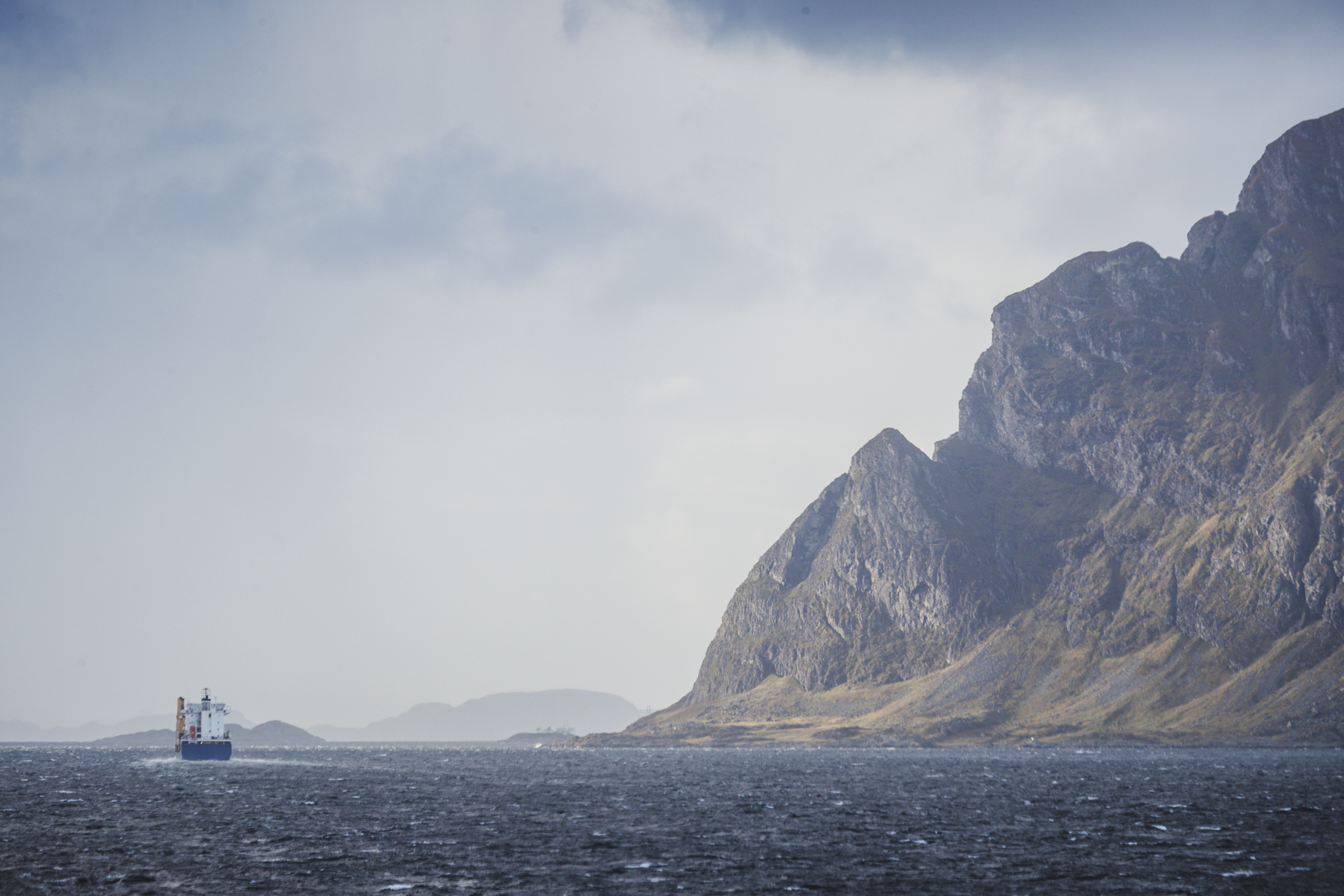 fiskefartøy i bølgete sjø forbi høye nakne fjell