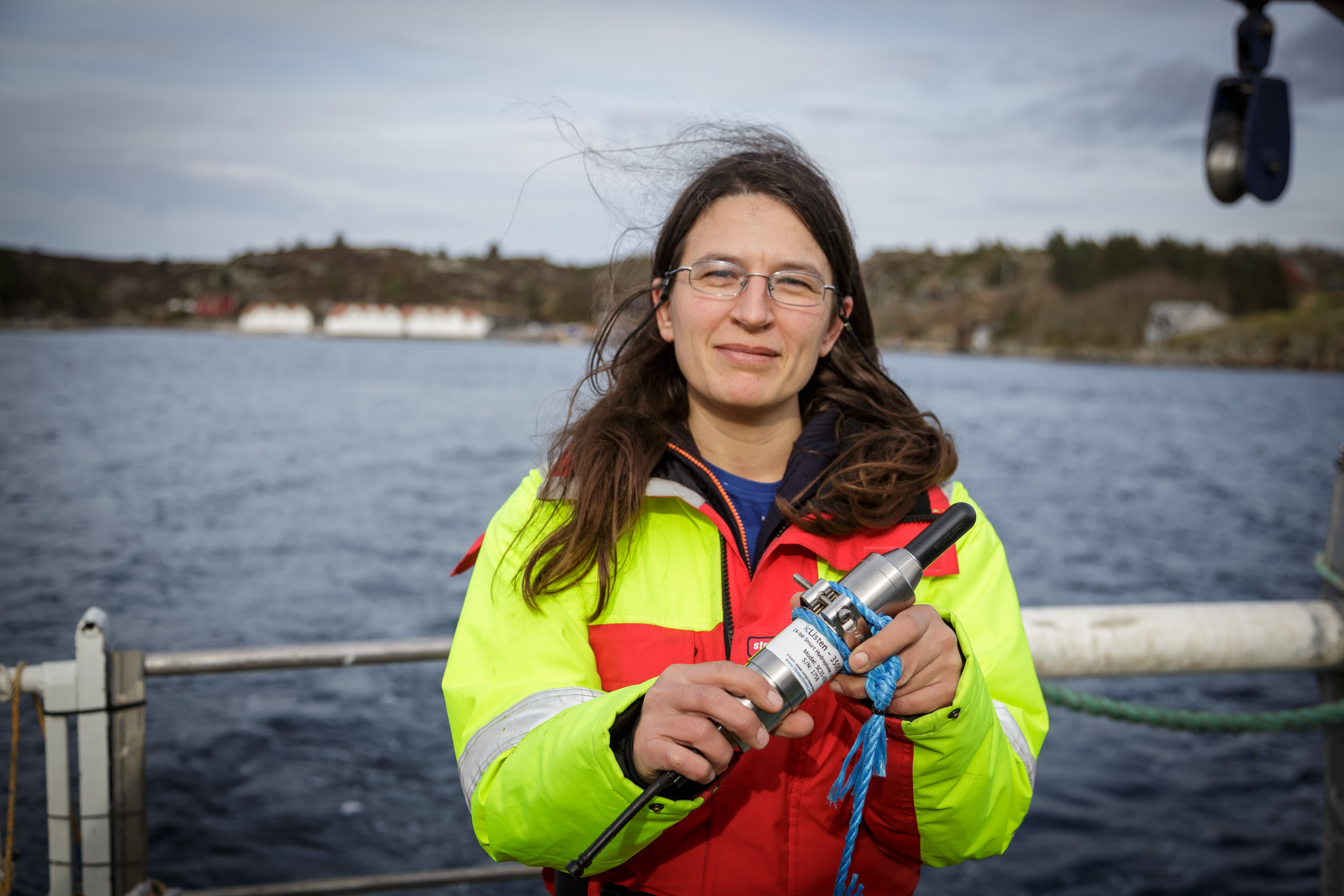kvinne i kjeledress i båt holder en avlang ting mot kamera