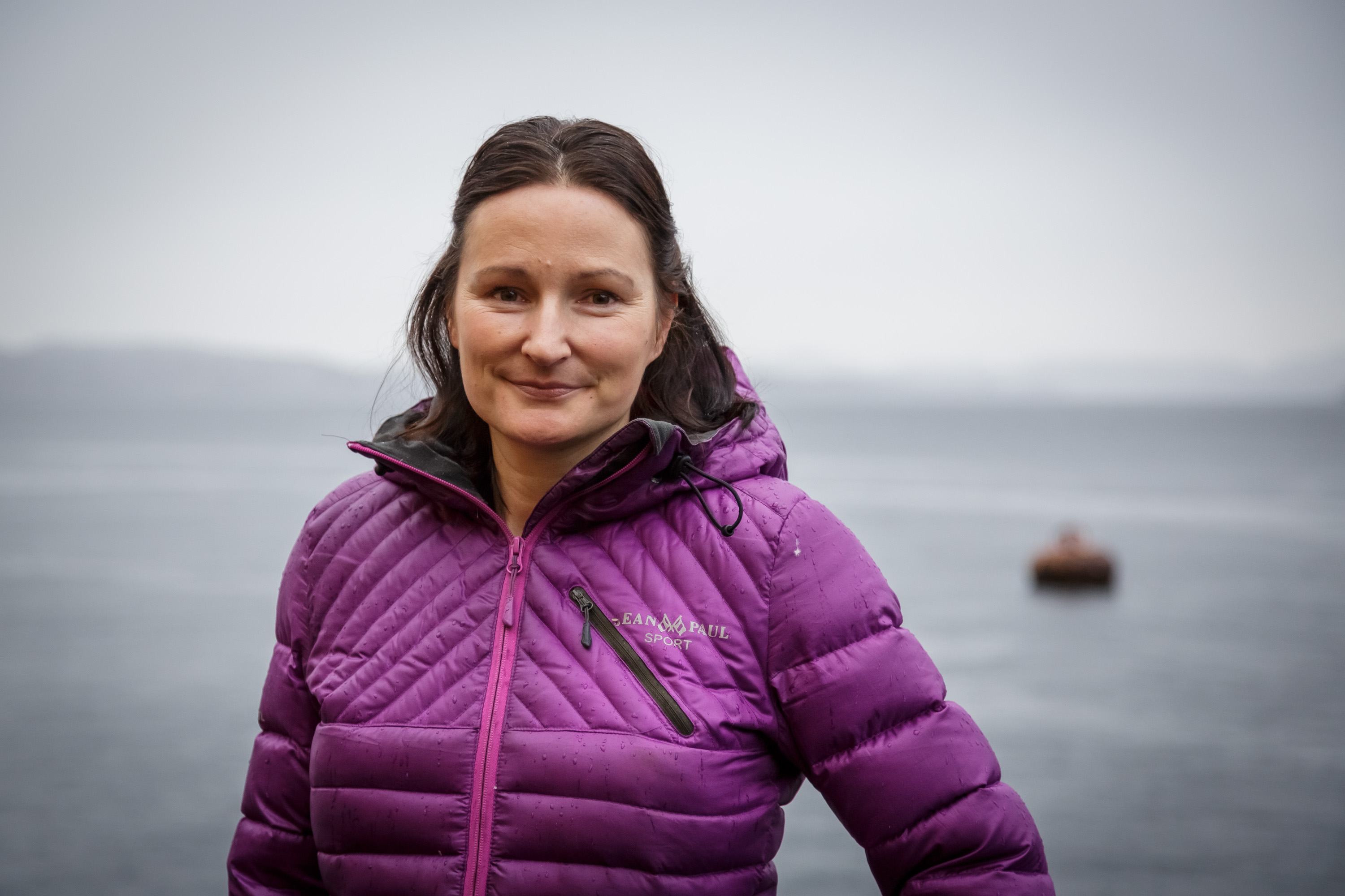 Kvinne i lilla boblejakke med fjord i bakgrunnen.