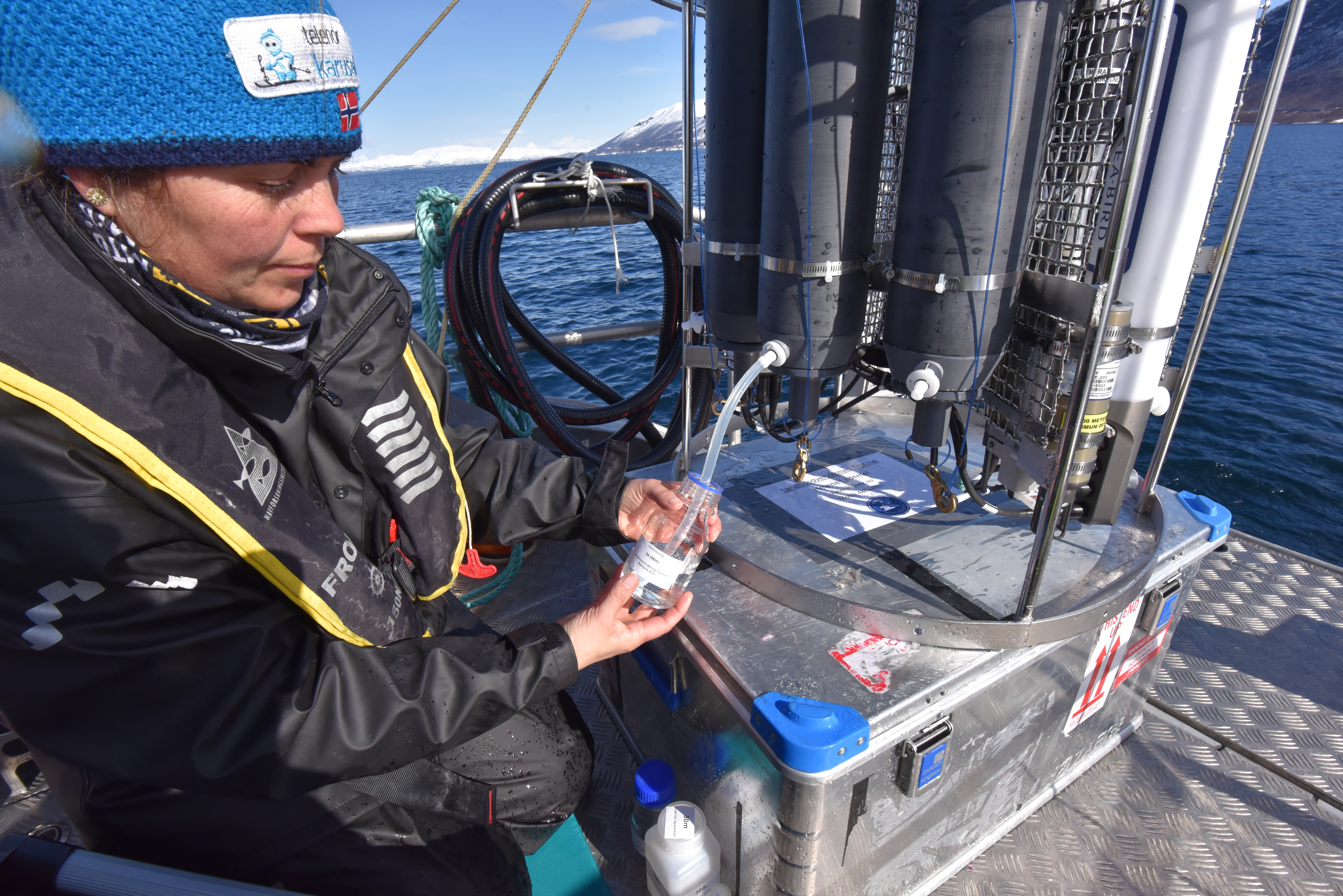 Kvinne med lue fyller en prøvetakingsflaske med vann fra vannhenterkransen.