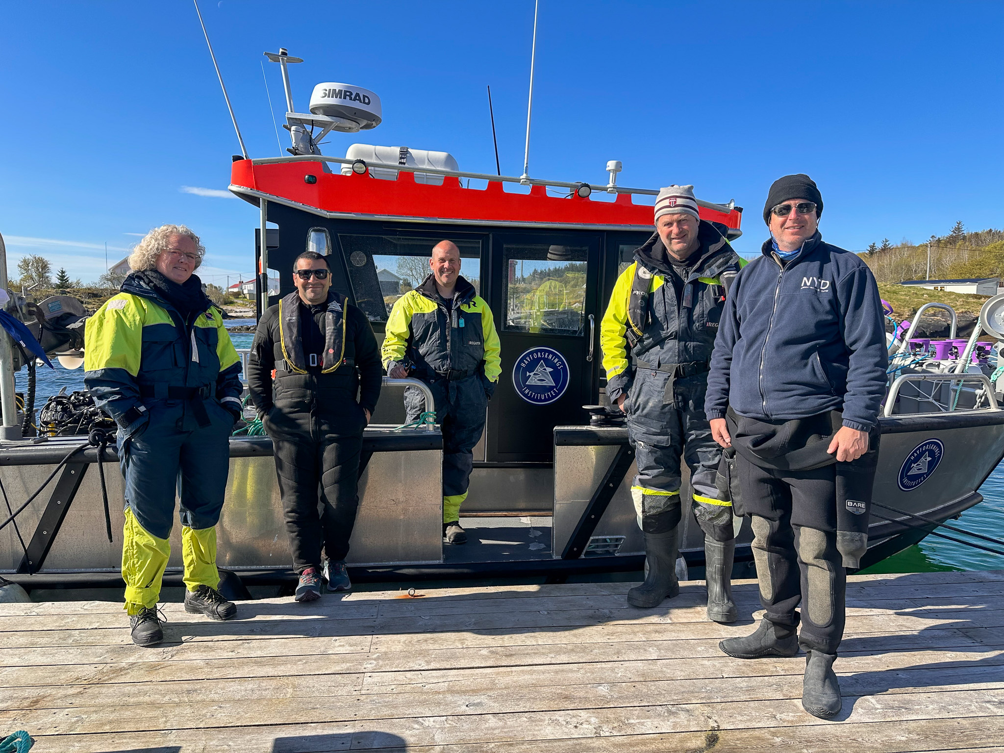 en kvinne og fire menn foran en båt