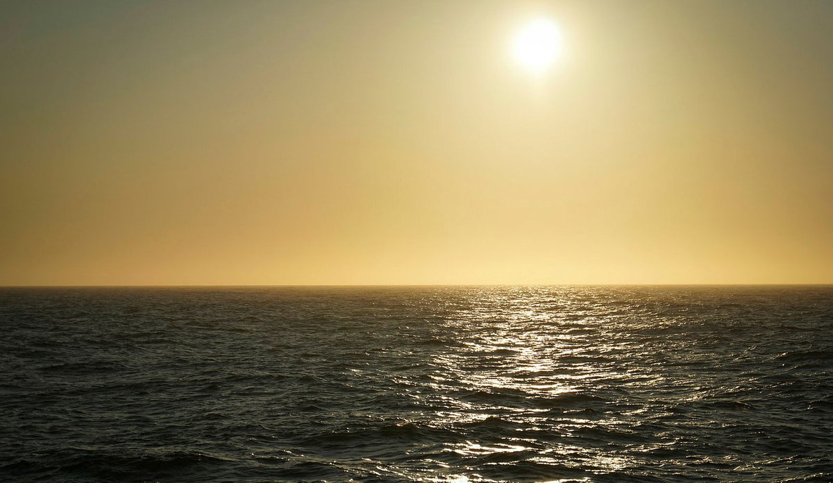 
Bildet viser midnattsol på skyfri himmel over stille vann.