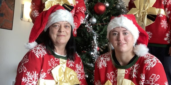 

Fire kvinner med røde julegensere og nisseluer og et juletre i bakgrunnen.