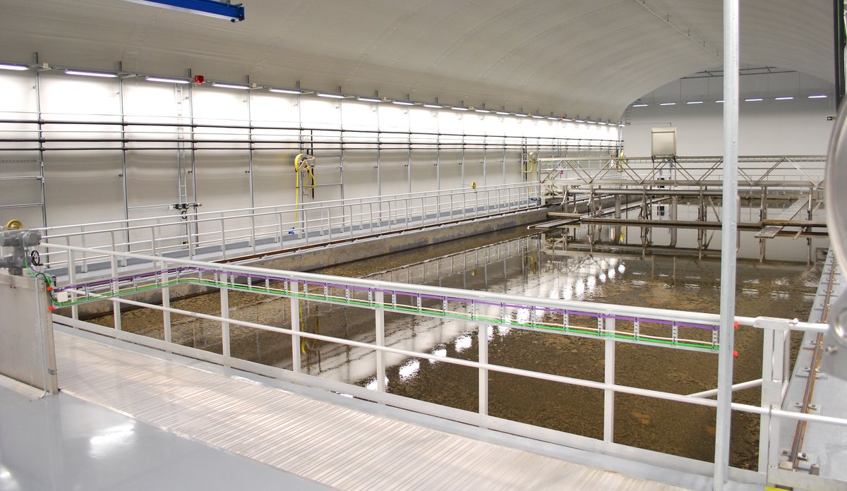 
Grå hall med rekkverk og stort basseng med brunaktig væske i midten.