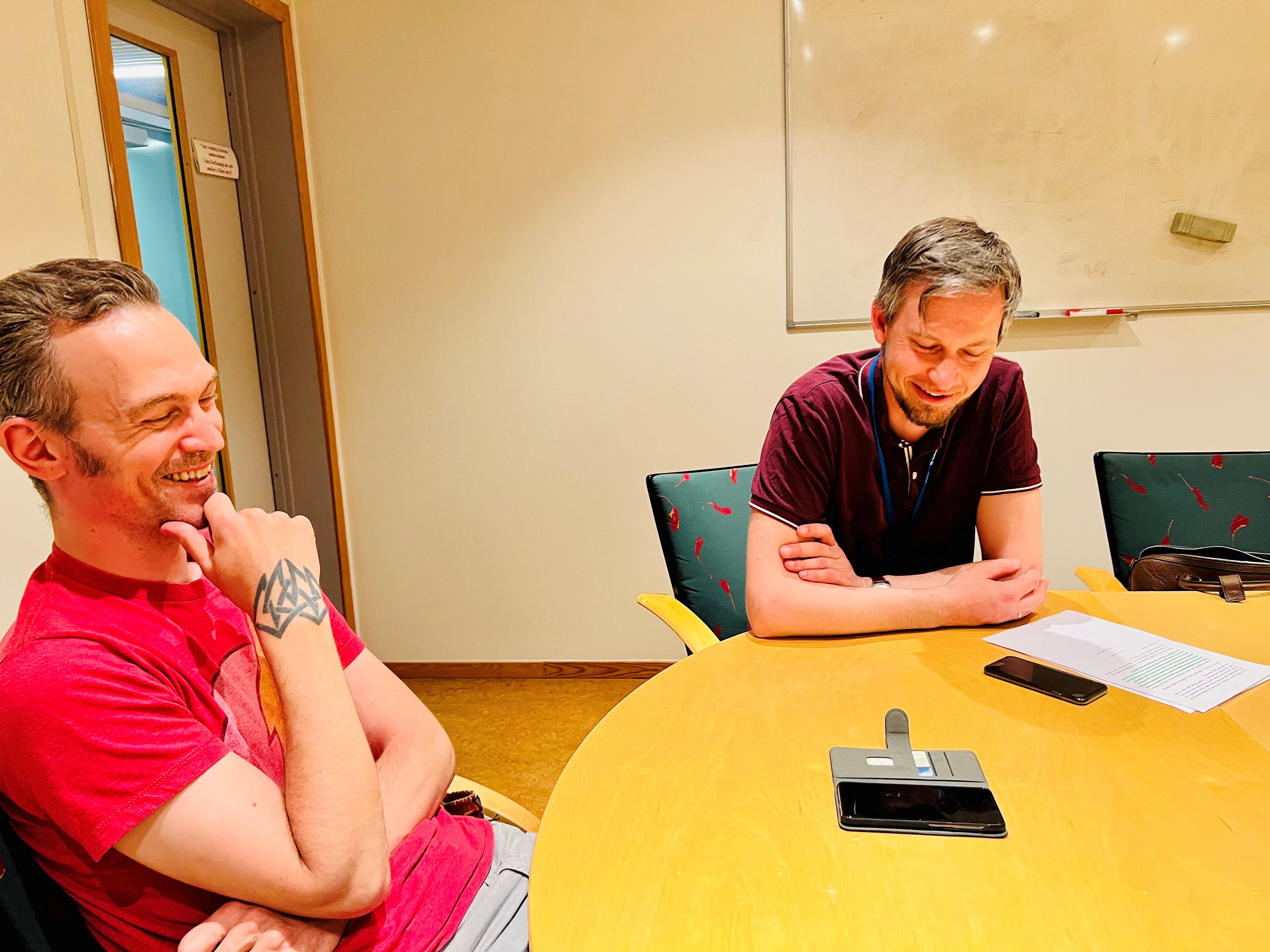 to menn i stoler ler, telefon på bordet foran de