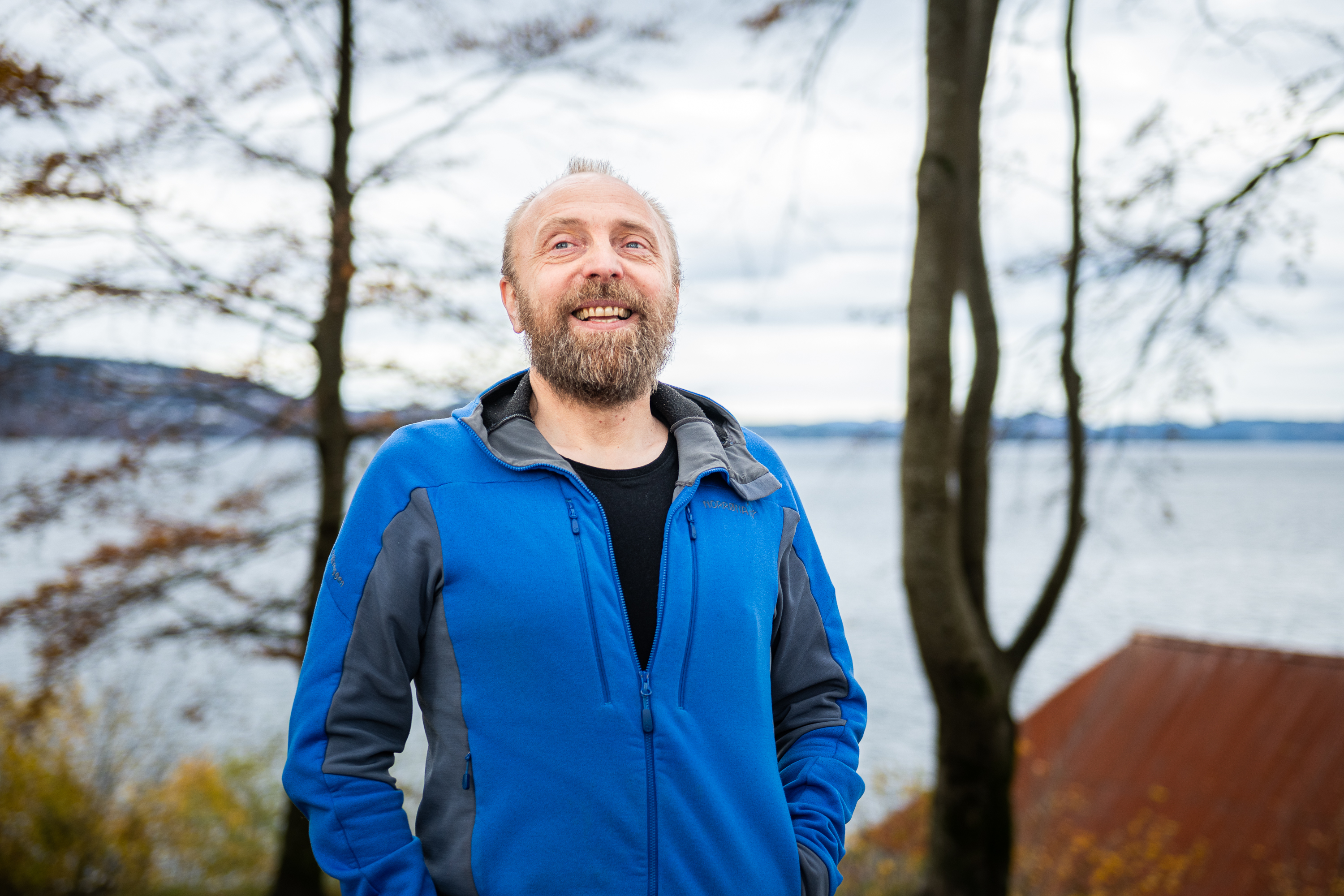 storsmilende mann i blå jakke ute i park