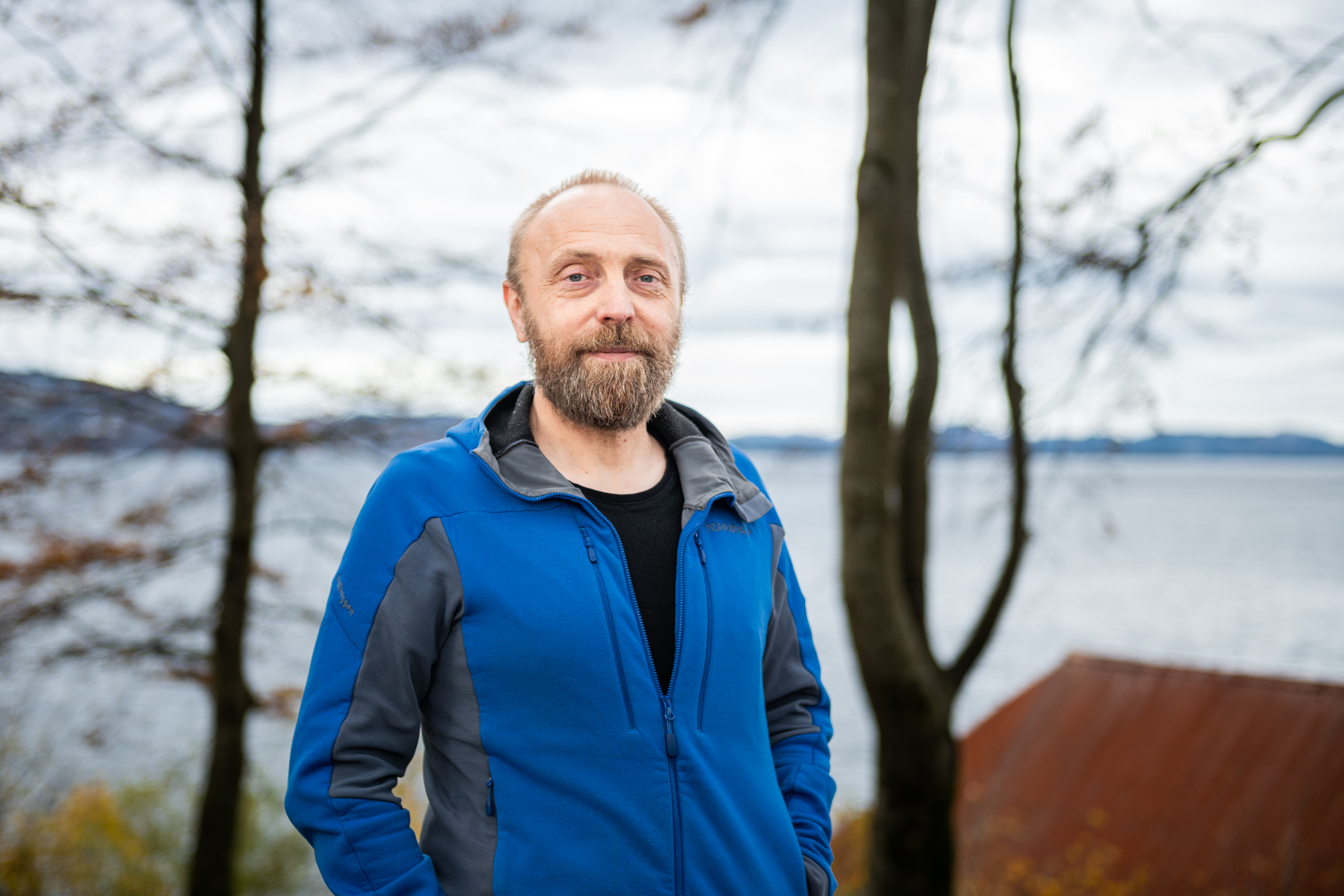 mann i fleecejakke med blått hav og tre i bakgrunnen