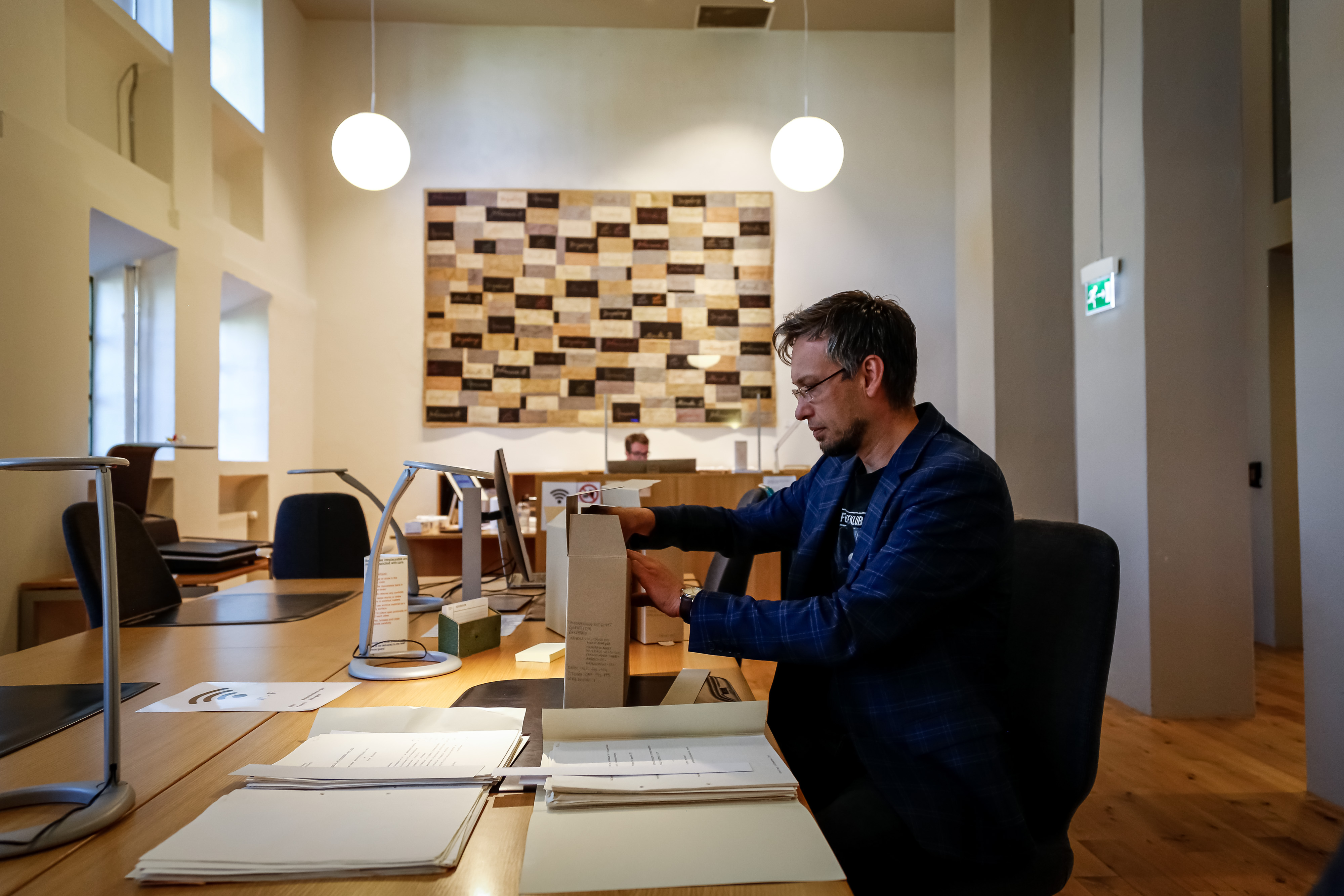 mann tar opp papirmappe fra pappkasse sittende i lesesal 