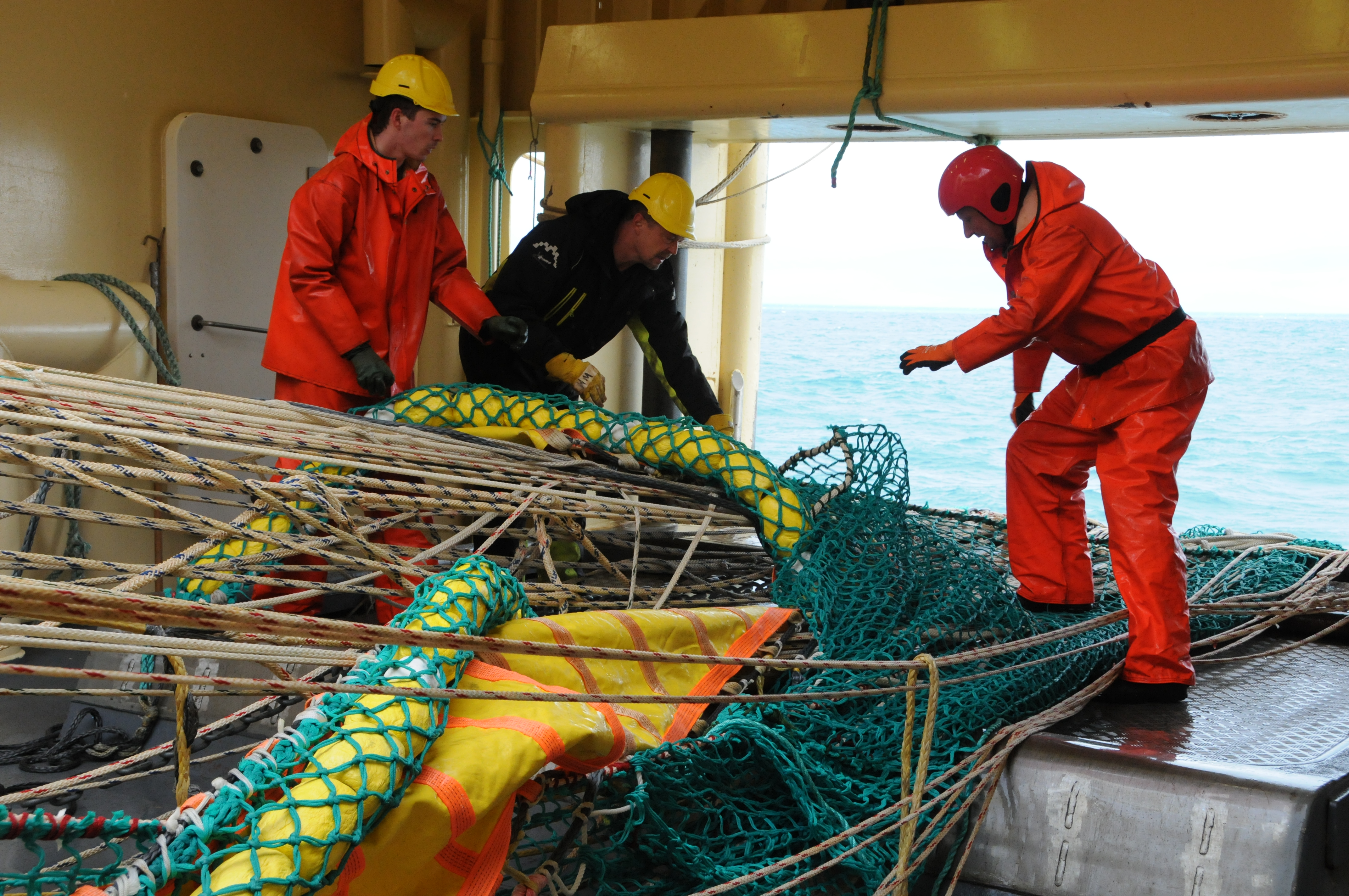 Tre personer jobber på et forskingsfartøy. De står ved siden av en luke på fartøyet, og er i ferd med å ordne kiten de nettopp har brukt til å tråle i overflaten.