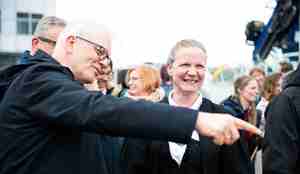 Dresskledd mann med briller peker ut av bildet, mens bunadskledd kvinne smiler