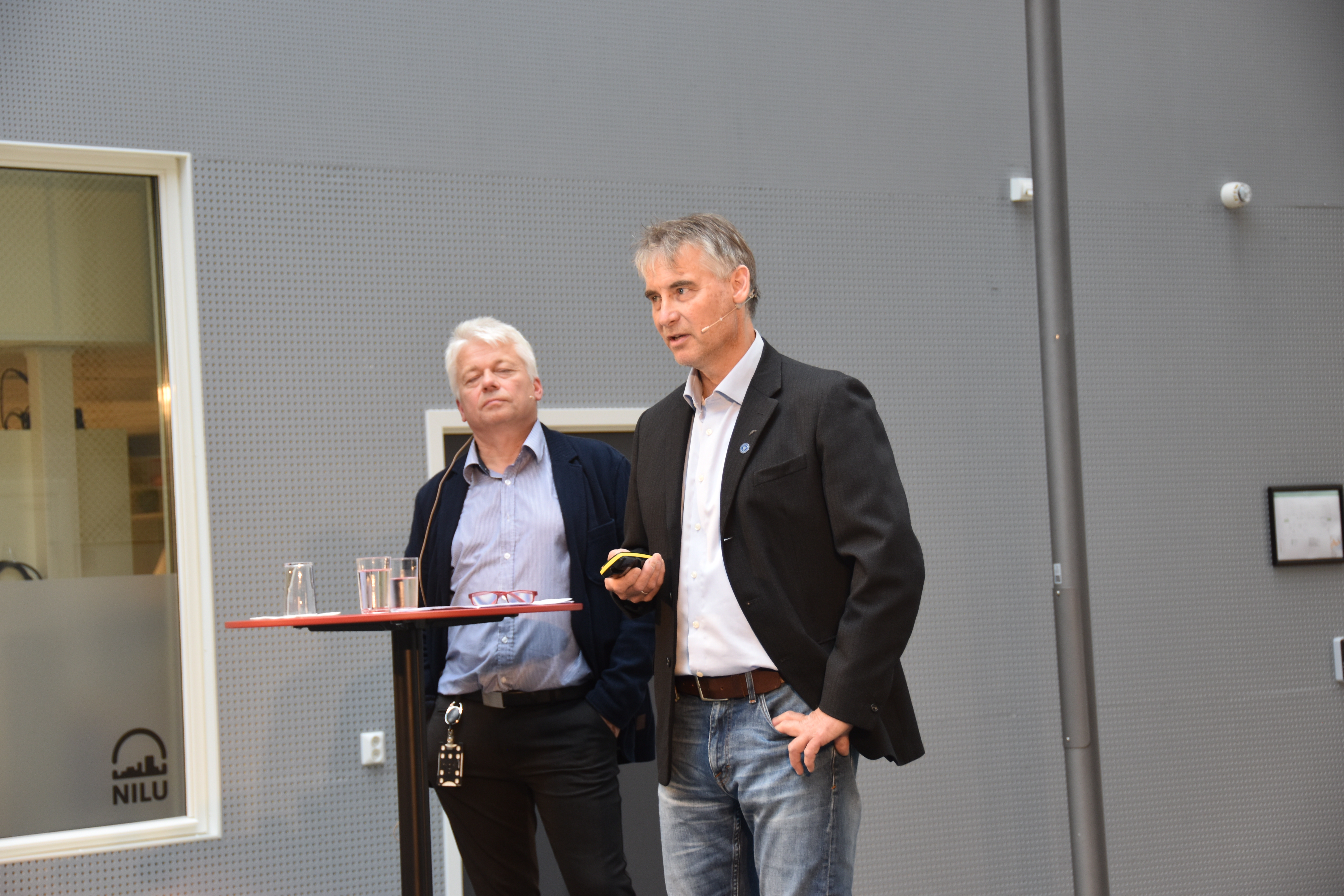 To menn på scene med storskjerm bak seg 