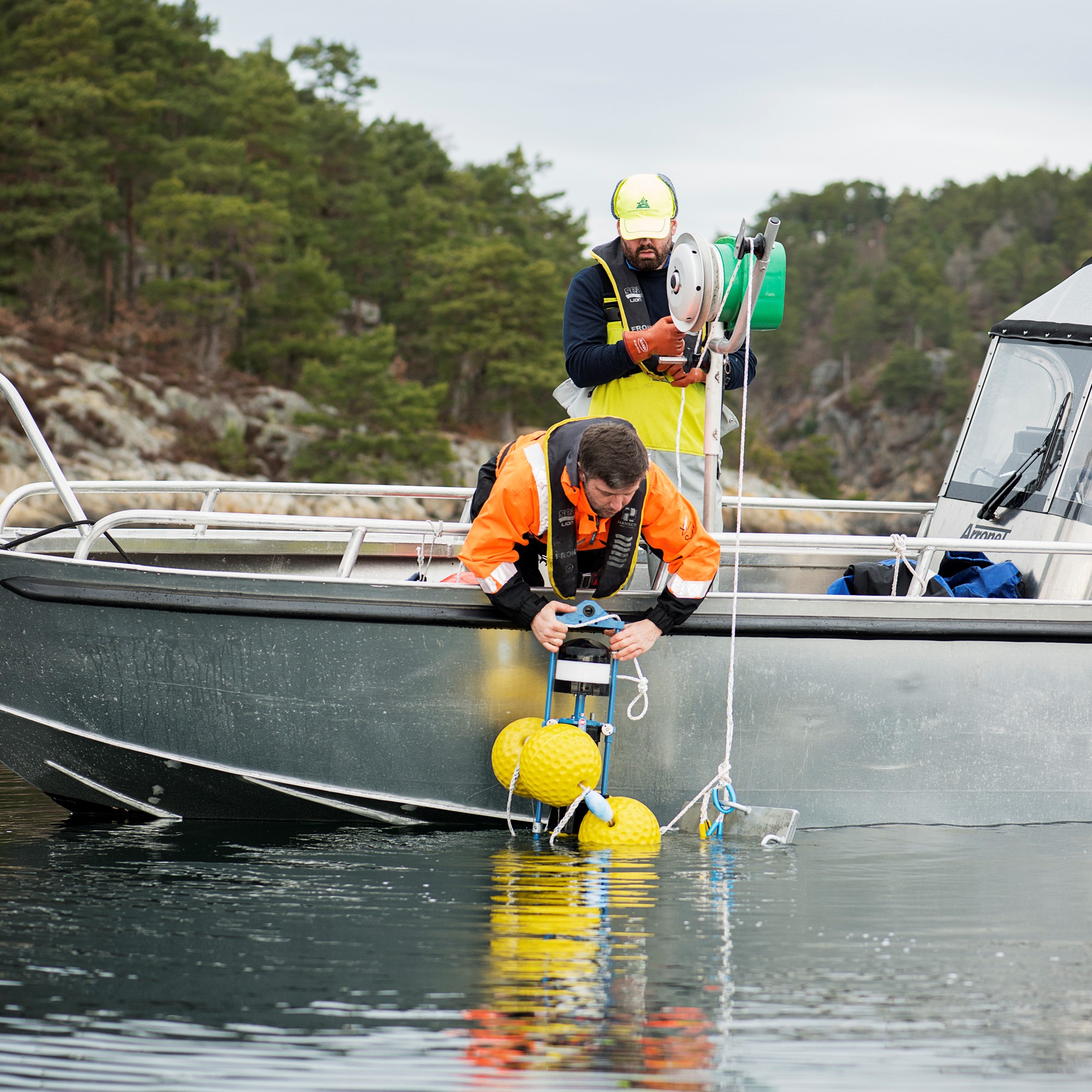 To menn bøyer ser over ripa på grå lettbåt for å plasser en strømmåler i sjøen.