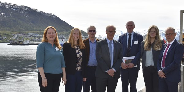 

Syv personer står oppstilt på en kai med utsikt mot havet bak seg. 