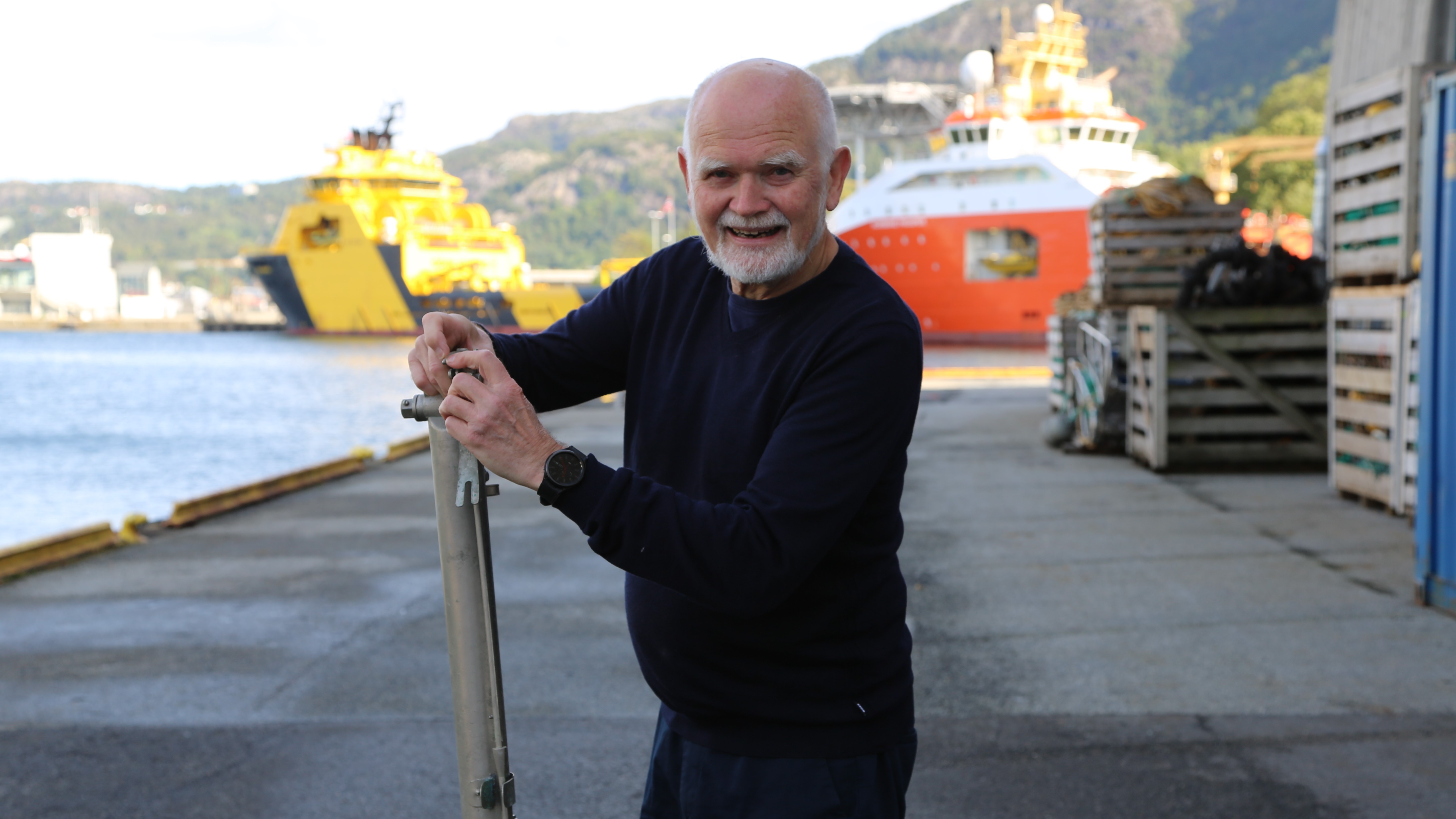 Havforsker Svein Sundby står på en kai med skip i bakgrunnen og viser frem en vannhenter.