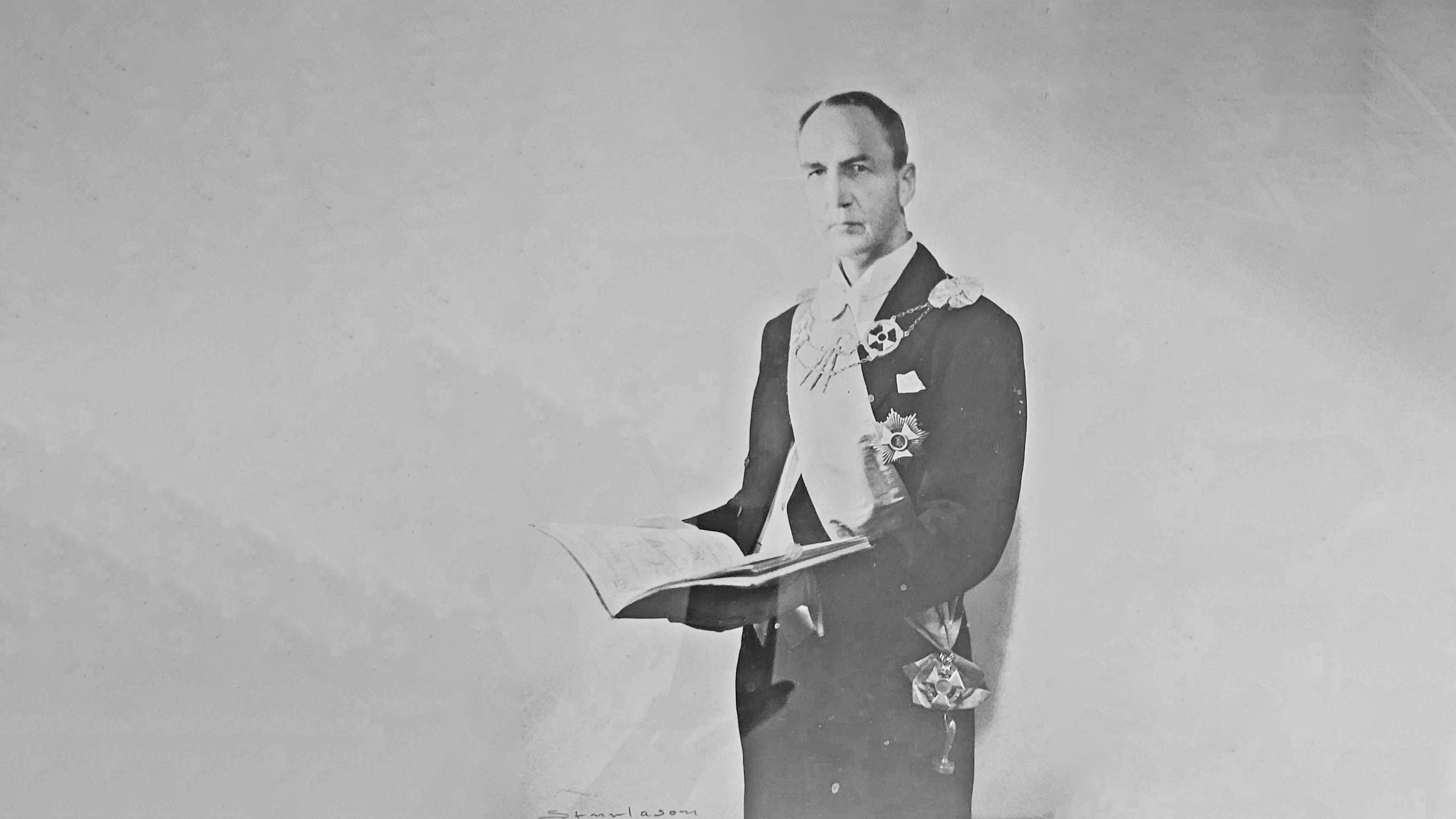 mann i pen dress med utmerkelser holder en bok 