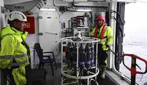 Mannskap står ved en CTD, som er en vannhenterkrets som senkes ned i vannet. Den består av et rundt stativ med flere små vanntanker festet til seg. 