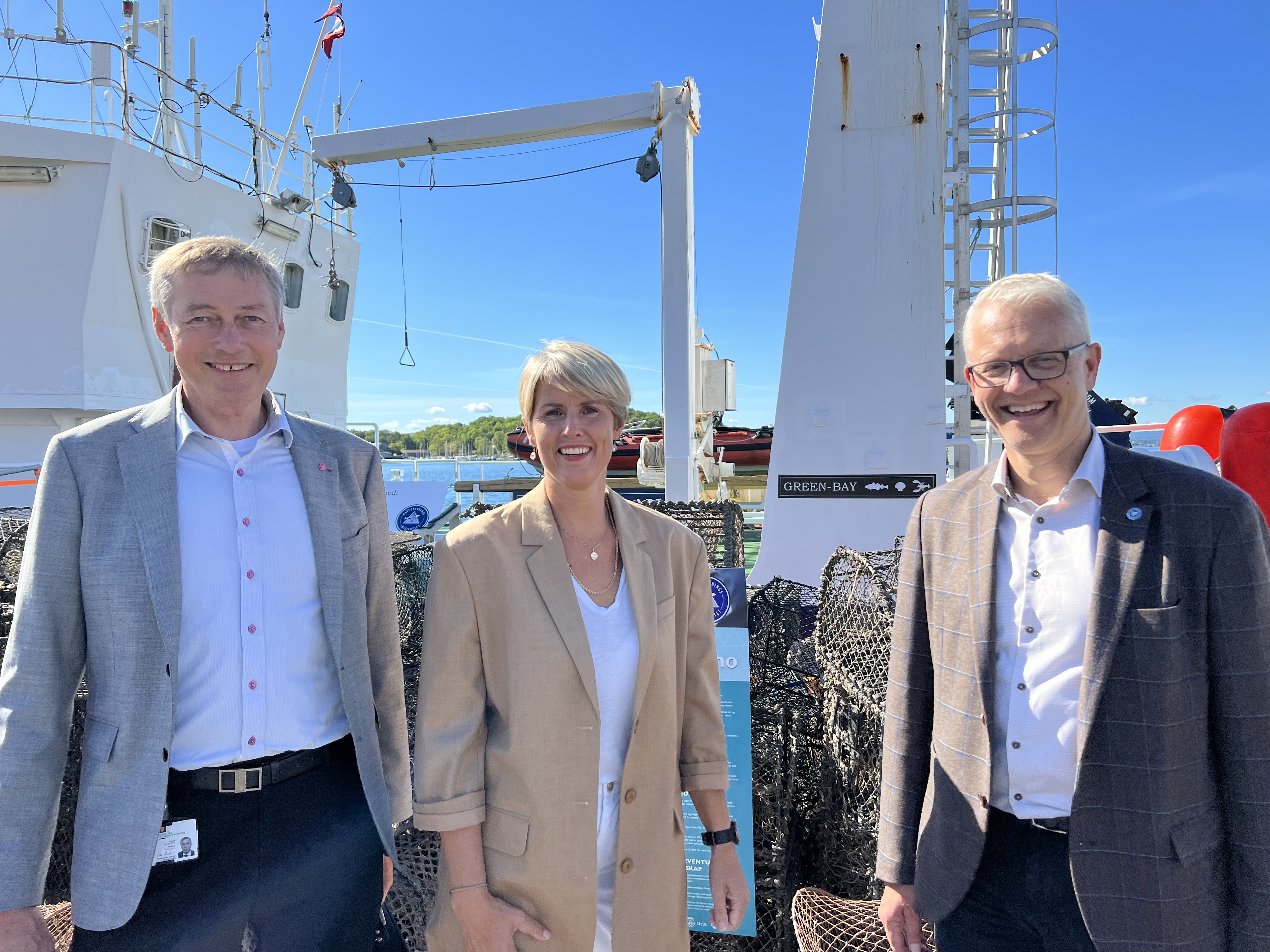 mann, kvinne og mann står smilende sammen foran en båt 