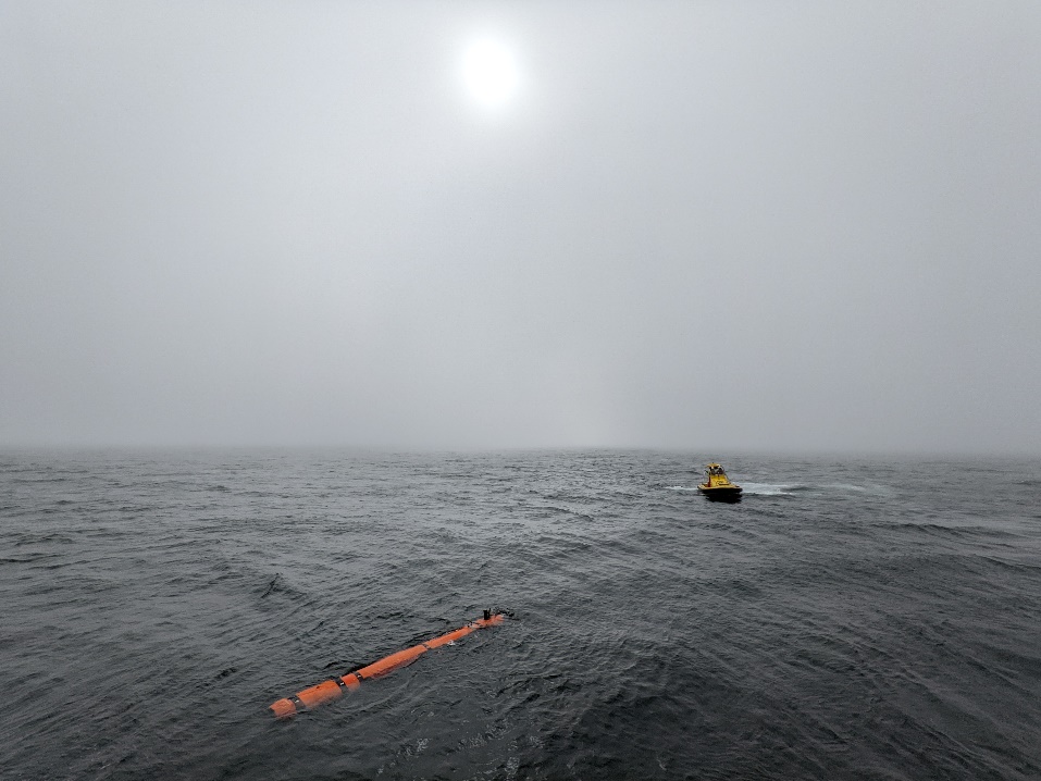 Photo of the AUV and MOB boat on calm water with fog obscuring the circle of the sun