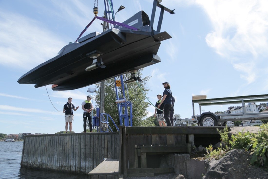 Bildet viser en båt som henger i luften og er i ferd med å sjøsettes. Båten er en hel-elektrisk, selvkjørende overflatedrone. 