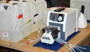 Fire plastkanner med slanger som går inn og ut av en maskin står på et bord inne i laben. Alt er fargekodet med teip. 