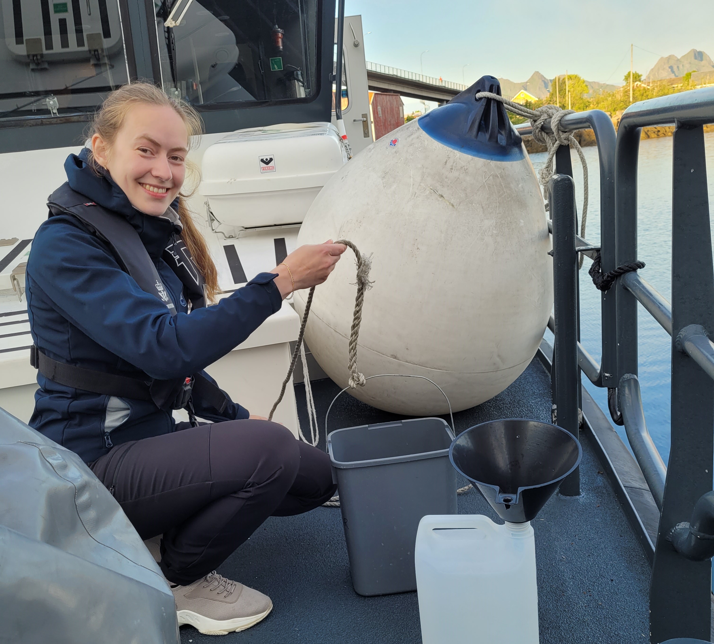 eg kvinne sitter på huk på dekk av en båt. Hun holder i et tau som er festet på en bøtte. Denne bøtta skal hun kaste over bord