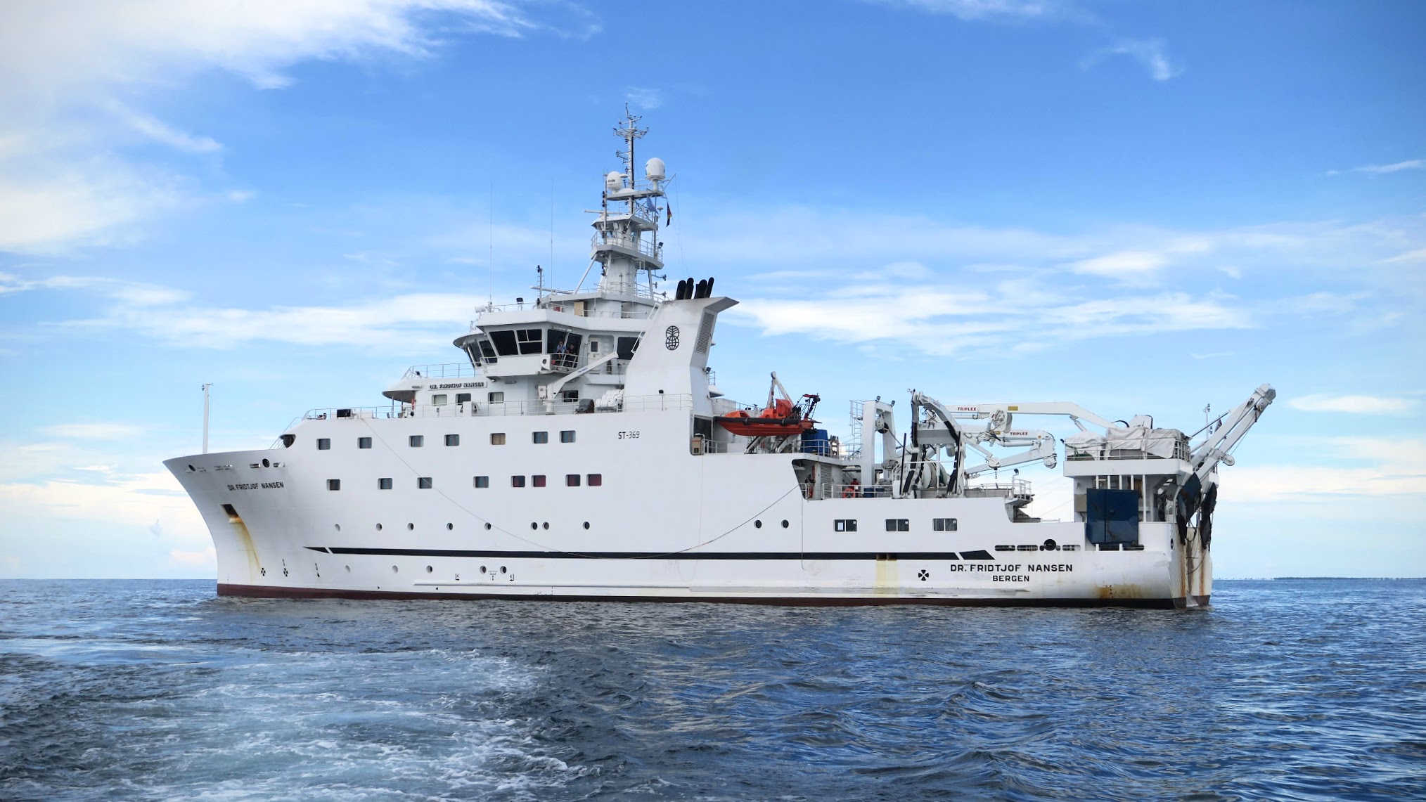 Stort, hvitt skip på blått hav og med blå himmel med noen spredte hvite skyer.