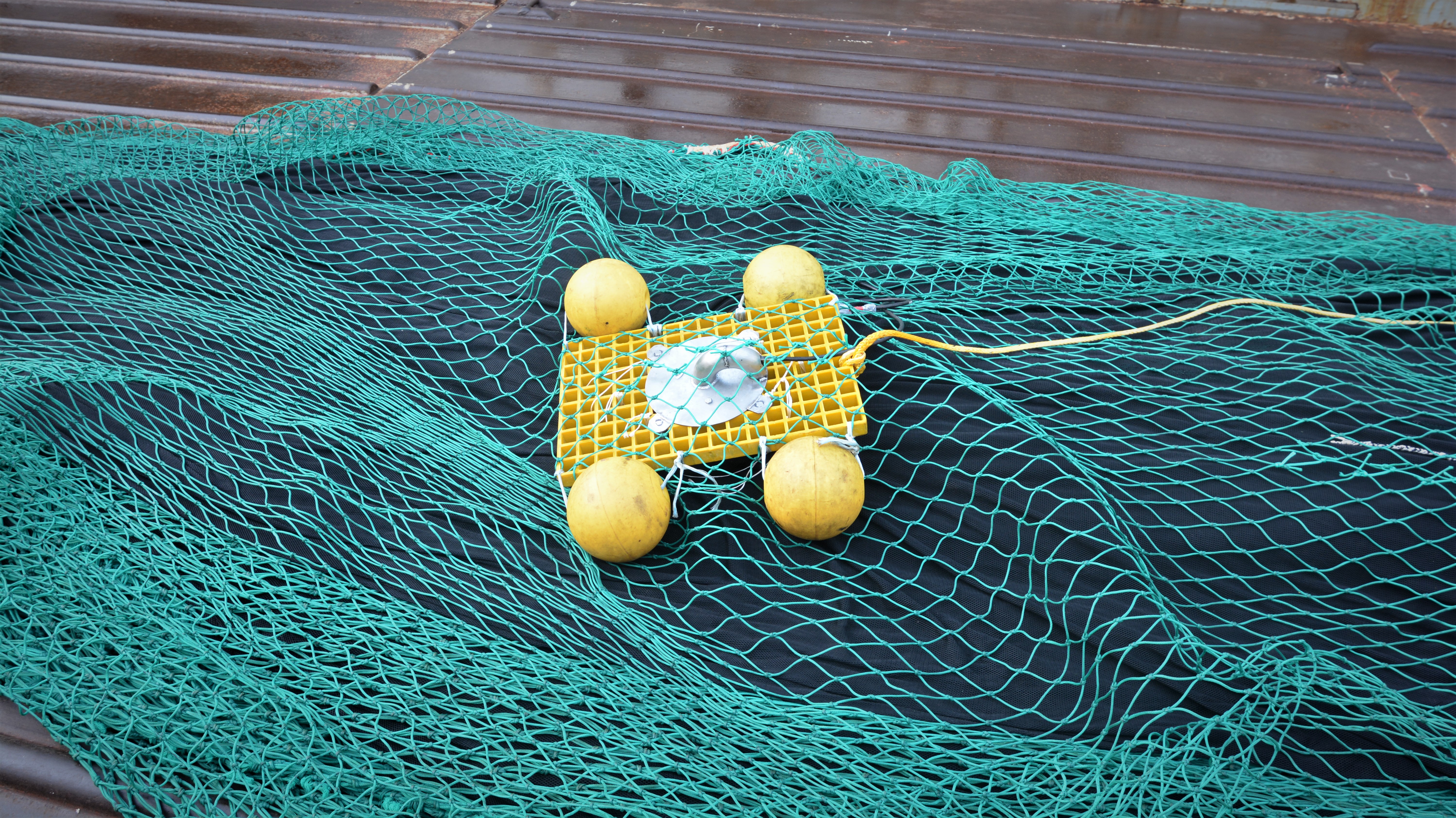 gul ting med gule blåser på, liggende oppå en sjøgrønn trålpose på skipsdekk