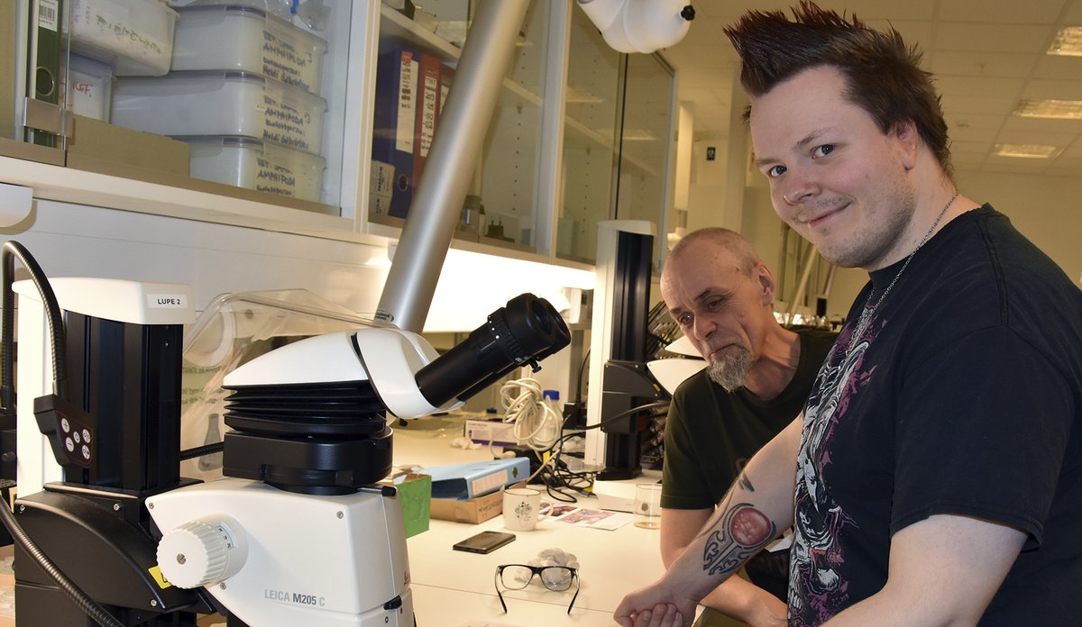 To havforskere ser i kamera og smiler. På bordet foran dem ligger en blekksprut som blir undersøkt.